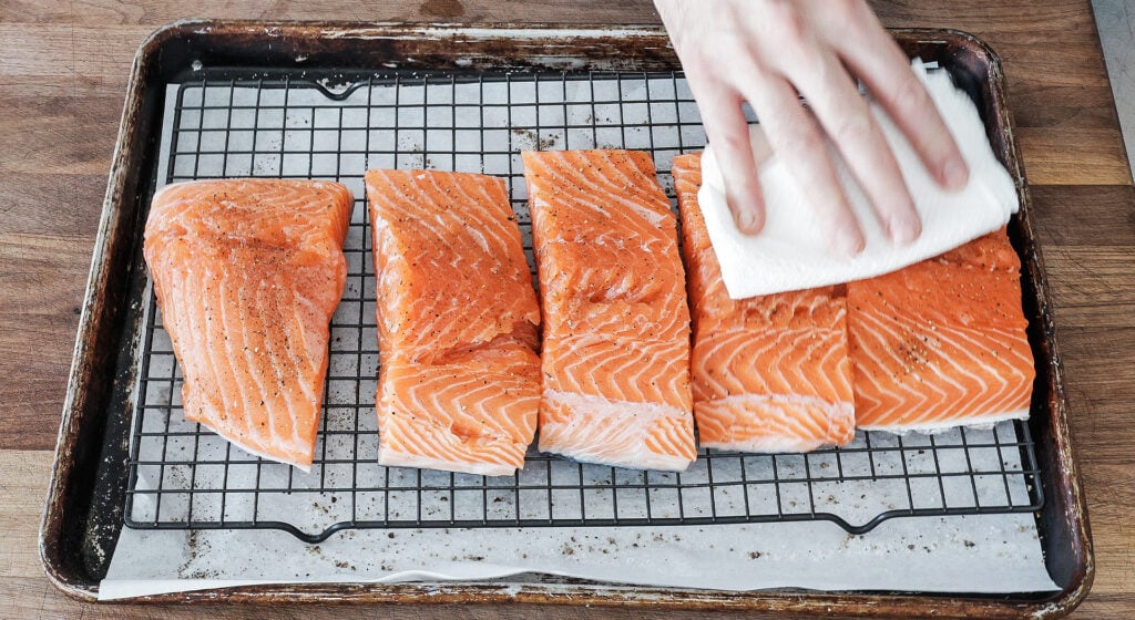 Salmon fillets being patted dry with a paper towel