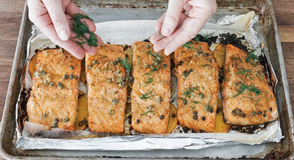 Baked salmon garnished with torn fresh dill on a citrus bed.