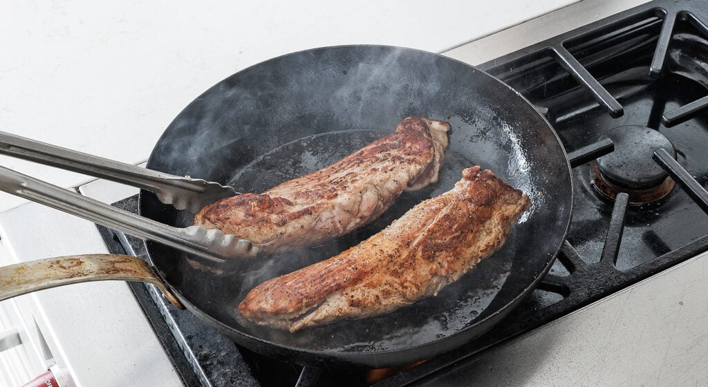 Pork tenderloins searing to a golden brown crust in a hot cast iron pan