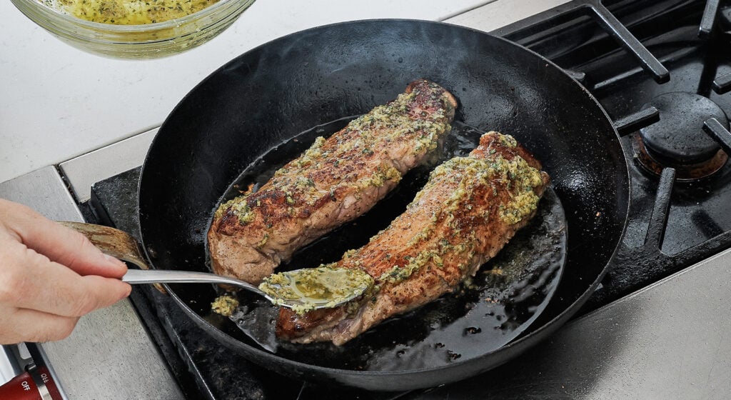 Seared pork tenderloins slathered with garlic herb marinade in a cast iron pan