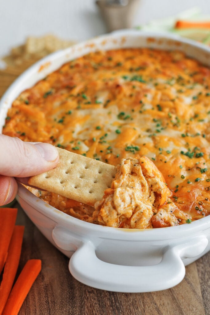 A cracker scooping a bite of cheesy buffalo chicken dip from the baking dish