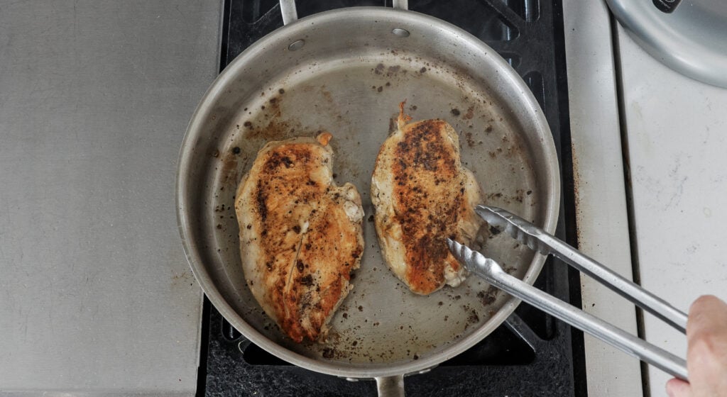 chicken breasts searing in olive oil in a saucepan
