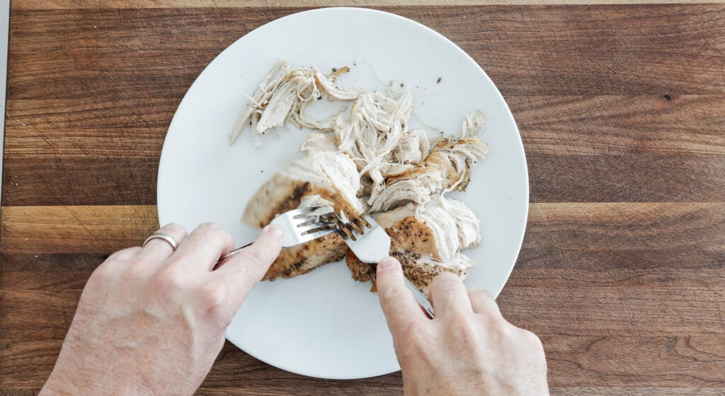 Cooked chicken breasts shredded with two forks on a plate 
