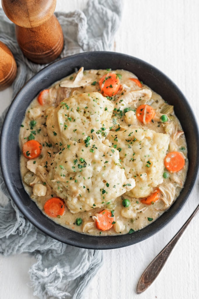 Chicken and dumplings in a shallow bowl with fluffy dumplings, herbs, and cracked pepper