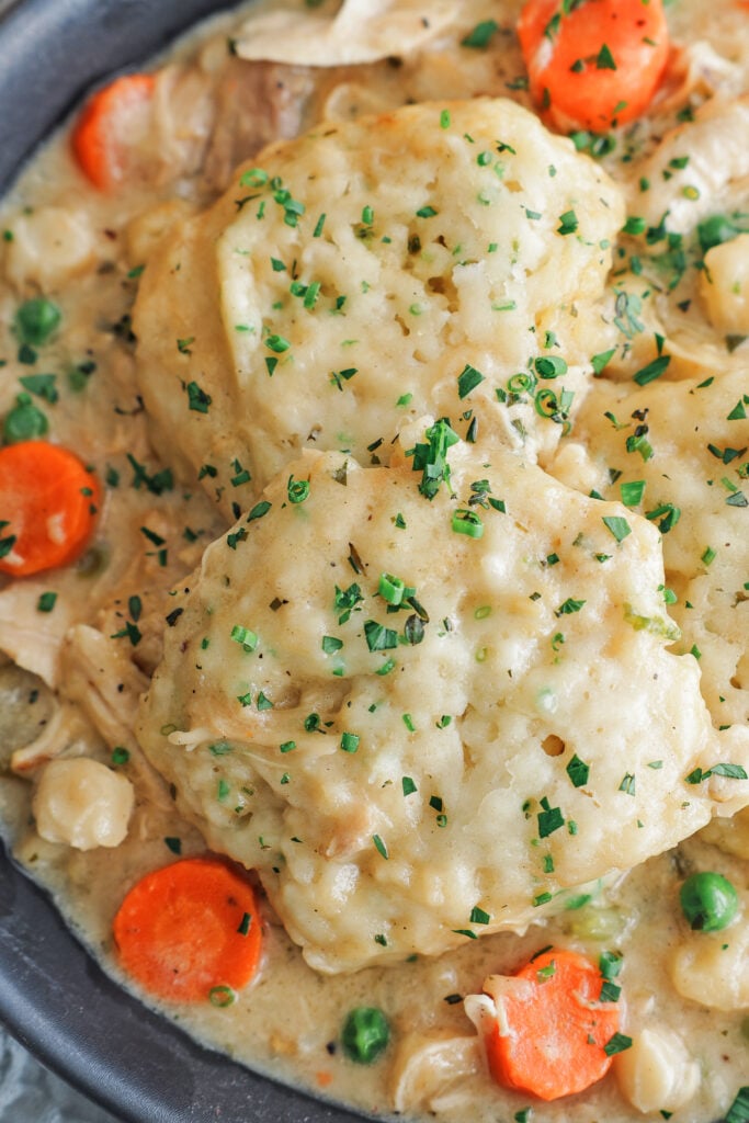 Chicken and dumplings in a shallow bowl with fluffy dumplings, herbs, and cracked pepper