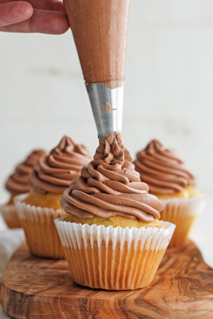 Piping chocolate Swiss buttercream onto a cupcake.