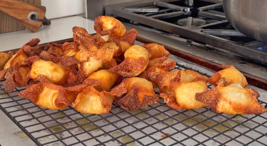 Fried crab rangoon draining and cooling on a wire rack set over a sheet tray