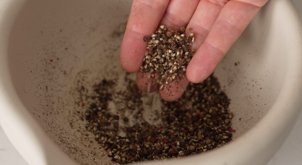 colored peppercorns toasting in a rondeau, then coarsely cracked in a mortar and pestle
