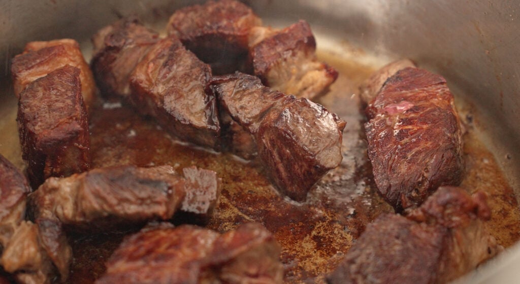 Cubed beef searing to a deep brown crust in a single layer in a hot rondeau