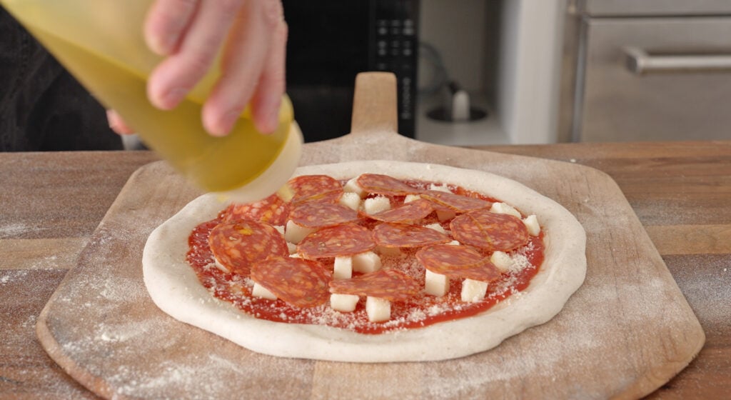 topping with raw San Marzano pizza sauce, cheese and meat