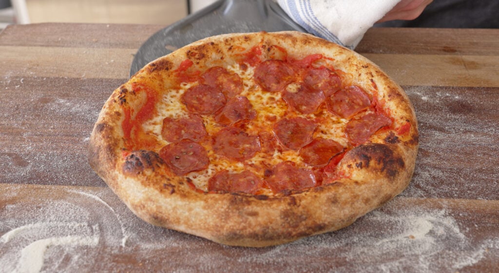 A baked sourdough pizza with a leopard-spotted airy crust, fresh mozzarella, on a wooden peel