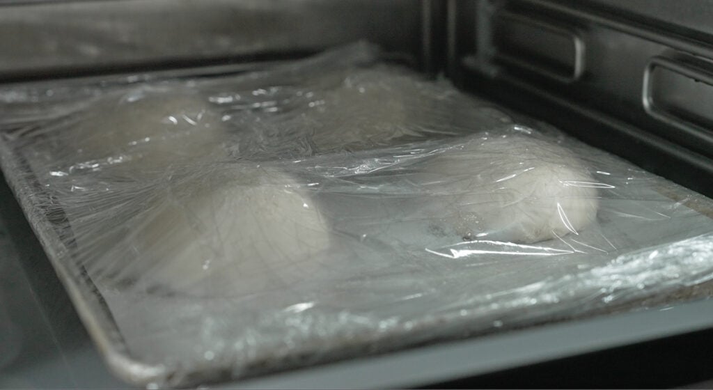 Four balled sourdough dough panetti resting on a parchment-lined tray for cold proofing
