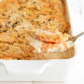 A spoonful of creamy sweet potato au gratin lifted from the casserole showing tender layered potatoes