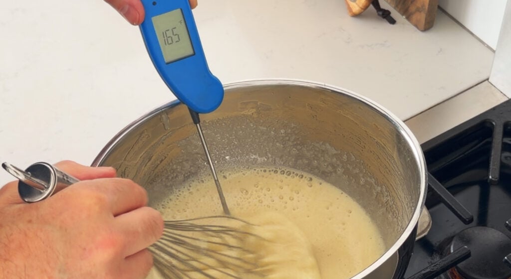 gg whites and sugar whisked in a glass bowl over simmering water
