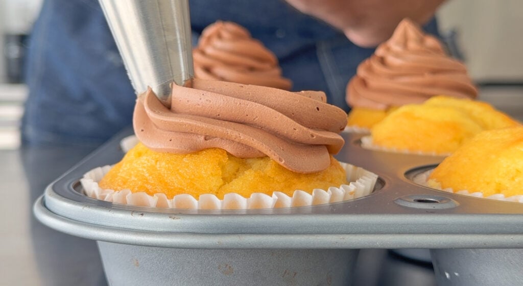 Piping chocolate Swiss buttercream onto a cupcake.