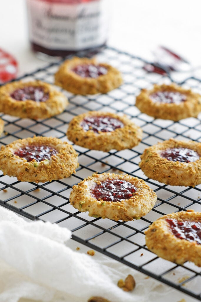 baked raspberry thumbprint cookies with golden edges cooling on a wire rack
