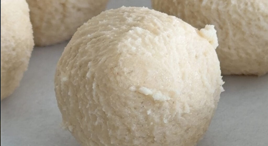 rolling shortbread dough into small olive-sized balls on a parchment-lined sheet tray
