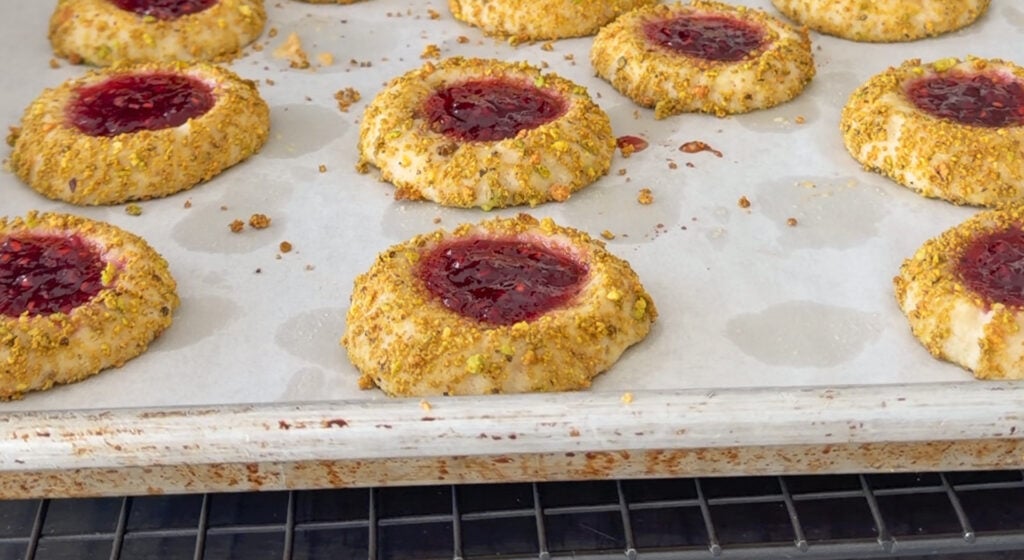 baked raspberry thumbprint cookies with golden edges cooling on a wire rack
